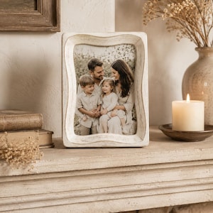 May include: A rectangular picture frame with a distressed white finish and a wavy, scalloped edge design. The frame holds a photograph of a family of four, including two adults and two children, all dressed in neutral-toned clothing outdoors.