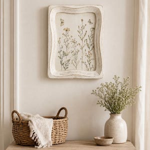May include: A rectangular wall art piece with a distressed white wooden frame featuring a botanical illustration of wildflowers and two butterflies on a cream background. The artwork is displayed vertically with a scalloped edge frame design.