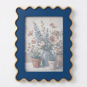 May include: A navy blue picture frame with a scalloped edge and a gold trim. The frame holds a painting of flowers in pots and a vase, with soft pinks, blues, and greens.
