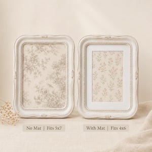 Op de afbeelding: Twee gebroken witte rechthoekige fotolijsten met kralenranden. De linkerlijst toont een beige bloemenprint en is gelabeld met 'No Mat | Fits 5x7'. De rechterlijst bevat een witte passe-partout, een roze bloemenprint en het label 'With Mat | Fits 4x6'.
