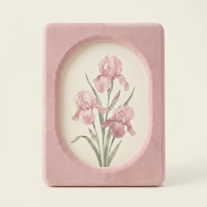 Könnte beinhalten: Ein rechteckiger, rosafarbener Samtfotorahmen mit ovaler Öffnung. Der Rahmen enthält ein Aquarell von drei rosa Irisblüten mit grünen Blättern und Stängeln. Der Hintergrund ist ein weiches Off-White.