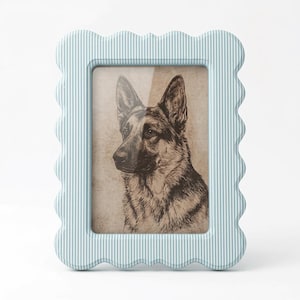May include: A pale blue picture frame with a scalloped edge and vertical white stripes. The frame contains a sepia-toned portrait of a German Shepherd dog. The frame is a decorative item.