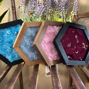 May include: Four hexagonal wall displays with wooden frames. Three frames contain textured, rose-patterned fabric in bright blue, light blue, and pink. The fourth frame features a dark burgundy velvet fabric with a gold celestial star and moon print.