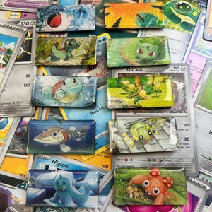 May include: A collection of ten rectangular glass cabochons featuring various colorful Pokémon illustrations, including characters like Bulbasaur, Squirtle, and Paras, arranged in two vertical columns over a background of assorted trading cards.