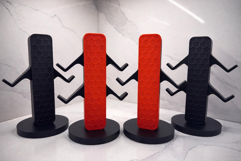 K&ouml;nnte beinhalten: Vier schwarze und rote Becherb&auml;ume mit modernem Design. Jeder Baum hat einen kreisf&ouml;rmigen Sockel, eine Mittels&auml;ule mit Wabenmuster und mehrere Arme zum Aufh&auml;ngen von Bechern. Die B&auml;ume sind aus mattem Material.