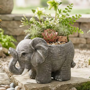 May include: A gray elephant-shaped planter filled with greenery, succulents, and small stones. The planter has a textured surface and white tusks. The plants include white and green flowers, and a red-tinged succulent. A decorative garden item.