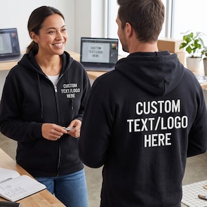 Puede incluir: Una sudadera negra con cremallera, texto blanco CUSTOM TEXT/LOGO HERE en el pecho izquierdo y texto grande blanco CUSTOM TEXT/LOGO HERE en la espalda. La sudadera incluye una capucha con cordones y una cremallera frontal completa.
