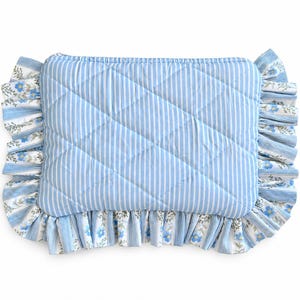 May include: A rectangular quilted cushion featuring a light blue and white vertical stripe pattern. The cushion is bordered by a ruffled edge that alternates between the blue and white stripe fabric and a floral print with blue flowers and green leaves.