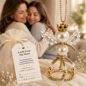 May include: A gold and white beaded angel ornament featuring a crown, pearl-like spheres, and clear crystal wings. A white gift tag is attached, printed with the text A Gift From The Heart, This little guardian is a reminder that someone is always thinking of you, With love, Little Guardian Co., To:, and From:.