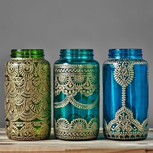 May include: Three glass jars with gold painted designs. The jars are teal, green, and blue. The jars are decorated with intricate patterns.