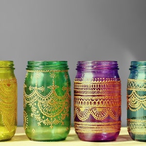 May include: Four glass jars with gold painted designs. The jars are painted in shades of green, yellow, purple, and blue.
