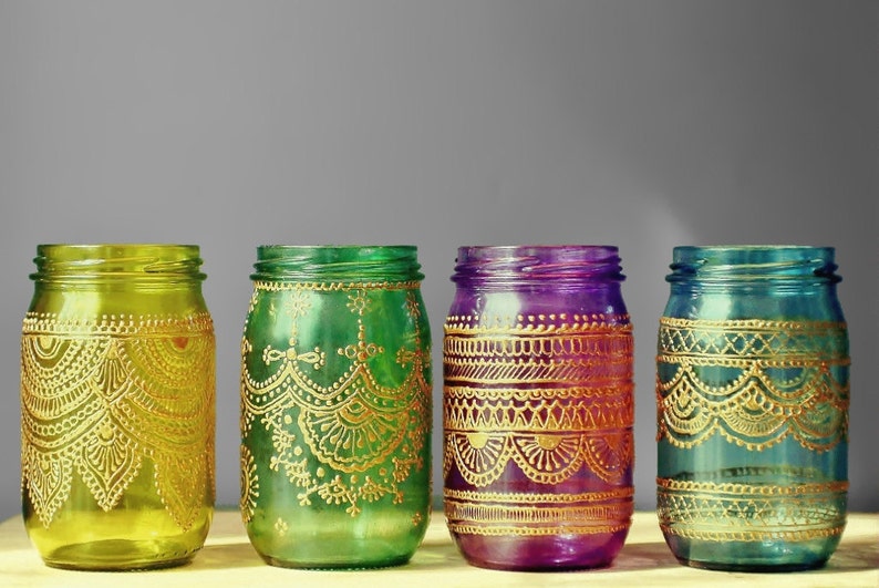May include: Four glass jars with gold painted designs. The jars are painted in shades of green, yellow, purple, and blue.