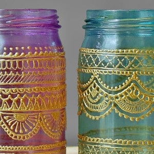 May include: Two glass jars with gold painted designs. The jar on the left is purple and the jar on the right is blue.