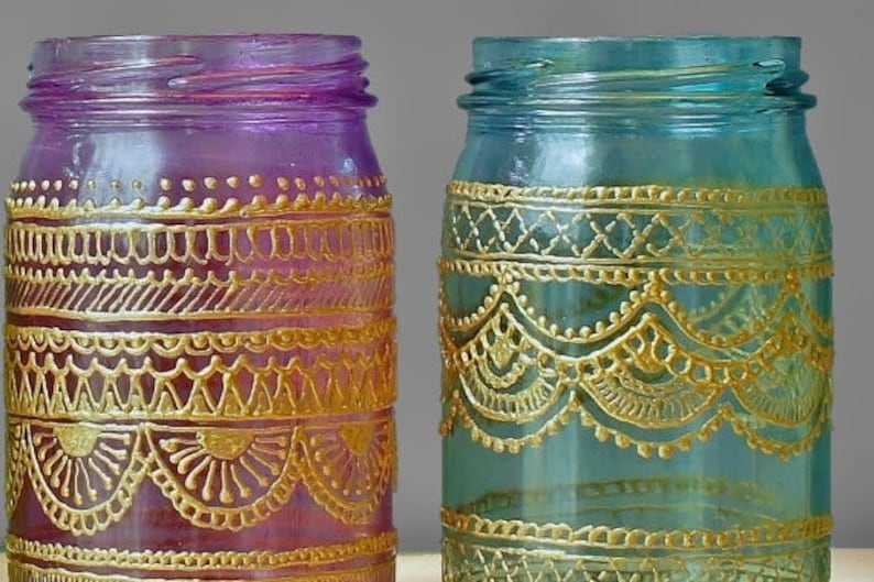May include: Two glass jars with gold painted designs. The jar on the left is purple and the jar on the right is blue.