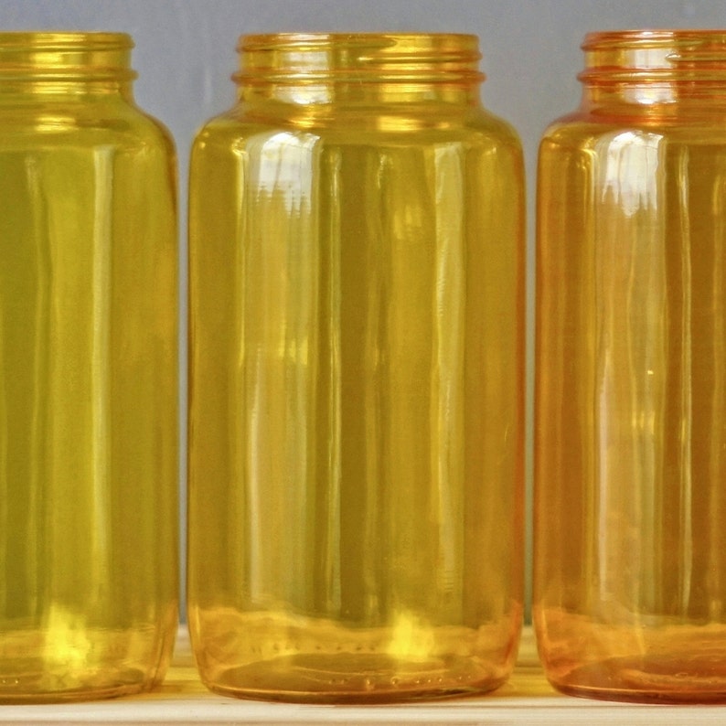 May include: Three amber glass bottles with a clear, slightly textured surface. The bottles are empty and have a cylindrical shape.