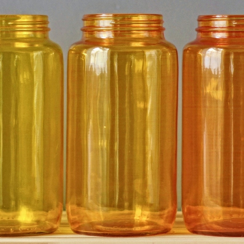 May include: Three glass bottles with a yellow, orange, and amber colour gradient. The bottles are clear and have a smooth, rounded shape.