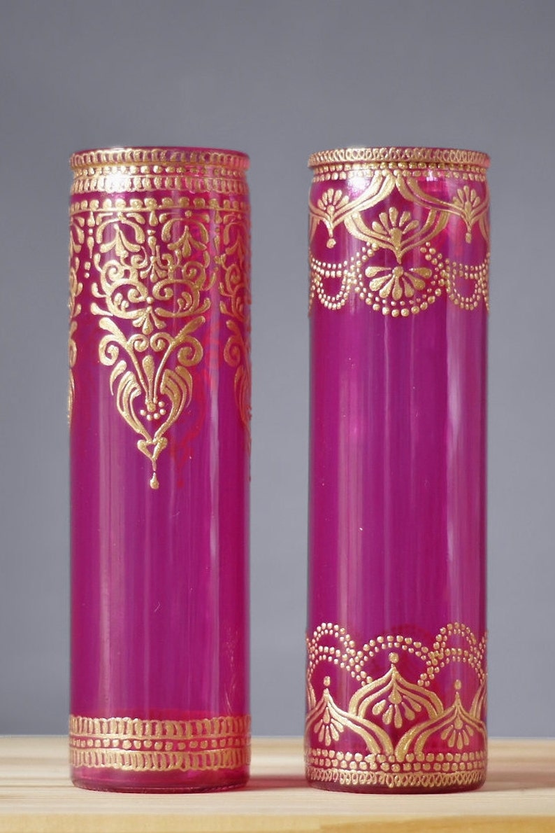 May include: Two magenta glass vases with gold painted designs. The vases are cylindrical and have a decorative gold band around the top and bottom.