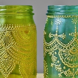 May include: Two glass jars with gold painted designs. The jar on the left is green and the jar on the right is blue.