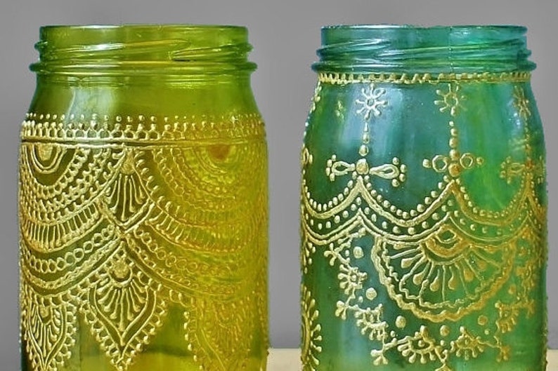 May include: Two glass jars with gold painted designs. The jar on the left is green and the jar on the right is blue.