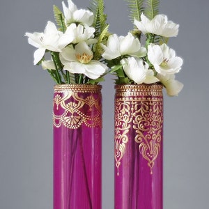 May include: Two magenta glass vases with gold painted designs, filled with white flowers.