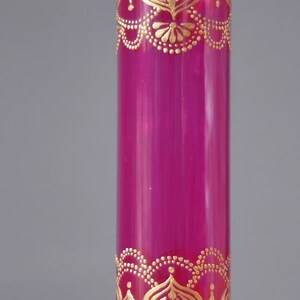 May include: A magenta glass vase with gold painted designs. The vase has a cylindrical shape and is decorated with intricate patterns.