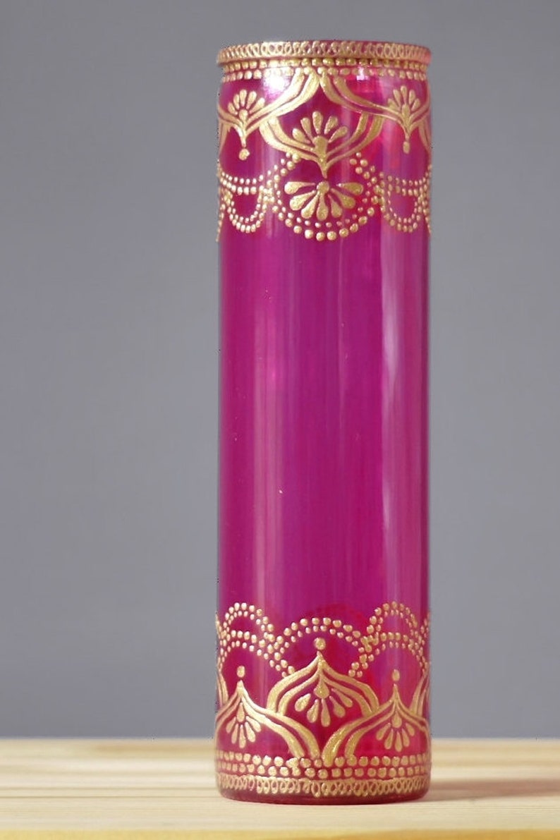 May include: A magenta glass vase with gold painted designs. The vase has a cylindrical shape and is decorated with intricate patterns.