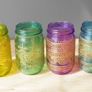 May include: Four glass jars with gold painted designs. The jars are in shades of yellow, green, purple, and blue.