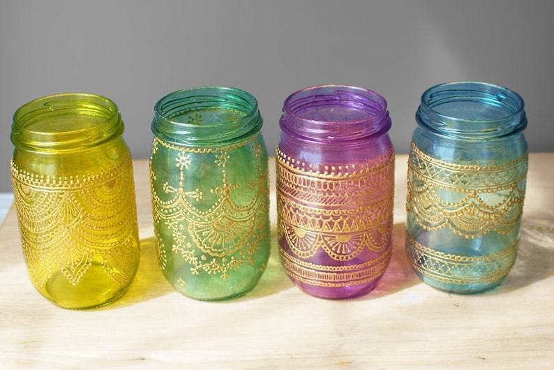 May include: Four glass jars with gold painted designs. The jars are in shades of yellow, green, purple, and blue.