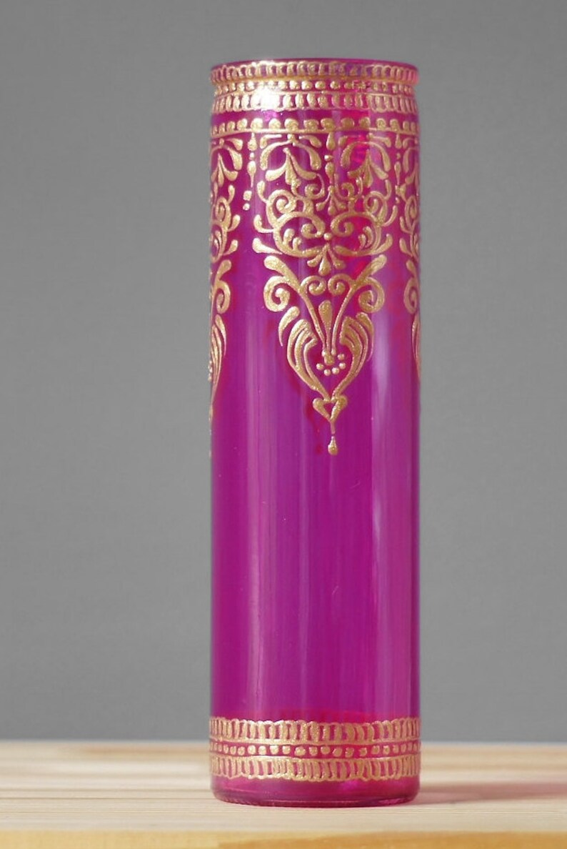 May include: A magenta glass vase with gold painted designs. The vase has a decorative pattern around the top and bottom.