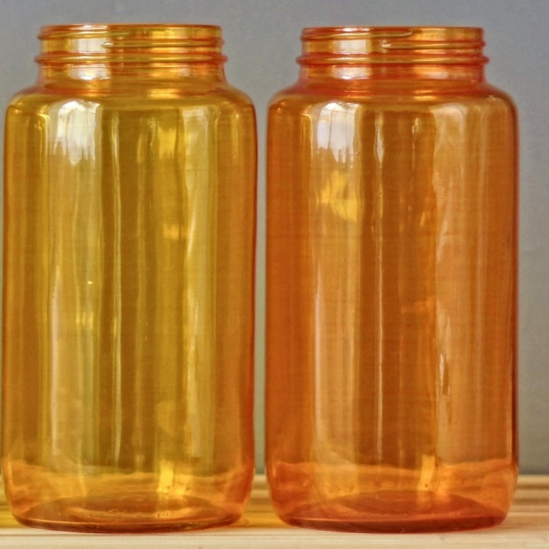 May include: Two amber glass bottles with a smooth, shiny finish. The bottles are empty and have a cylindrical shape.