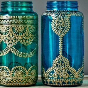 May include: Two teal blue glass jars with gold painted designs. The jars have a decorative, intricate pattern of gold paint.