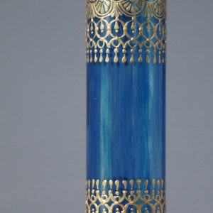 Op de afbeelding: Een blauwe glazen vaas met gouden beschilderde ontwerpen. De vaas heeft een cilindrische vorm en is versierd met ingewikkelde patronen.