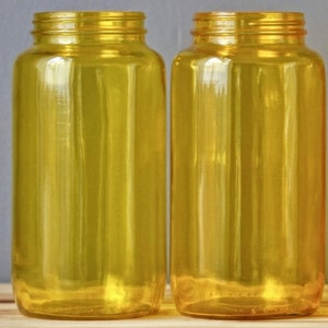 May include: Two clear glass bottles with a yellow tint. The bottles are empty and have a smooth, rounded shape.