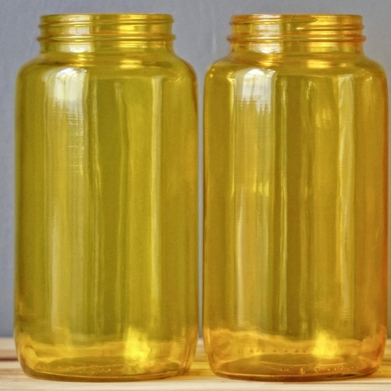 May include: Two clear glass bottles with a yellow tint. The bottles are empty and have a smooth, rounded shape.