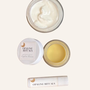 May include: An overhead shot of beauty products, including a jar of white cream, a small white jar with a label, and a lip balm. The label reads "OPALINE RITUALS" and "Opaline Bloom". The lip balm also has the brand name printed on it.