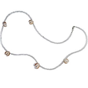 May include: A long necklace featuring a strand of small, clear, translucent beads interspersed with five evenly spaced, smooth, tan and white cowrie shells. The necklace is secured with a small silver-toned metal lobster claw clasp closure.