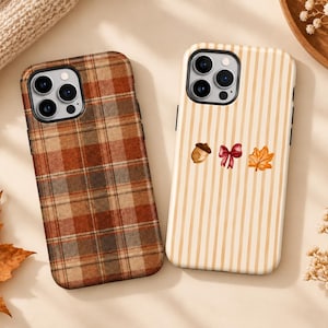 May include: Two smartphone cases. The left case features a brown, orange, and tan plaid pattern. The right case has vertical tan stripes and a small graphic print of an acorn, a red ribbon bow, and an orange maple leaf centred on the back.
