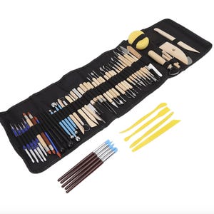 May include: A comprehensive pottery tool set featuring a black fabric roll-up organiser containing numerous metal and wooden sculpting tools, a yellow sponge, four yellow plastic modelling spatulas, and five brushes with dark brown handles.