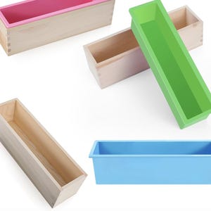 May include: A selection of soap molds in different colours and designs. The image displays rectangular wooden molds with silicone inserts in pink, green, and blue. The wooden molds are light brown, and the silicone inserts are bright.
