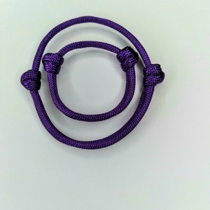 May include: A purple braided rope bracelet with two knots on each end.