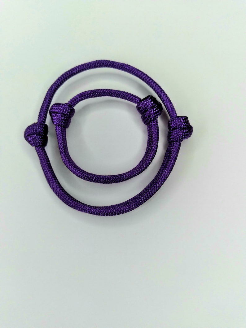 May include: A purple braided rope bracelet with two knots on each end.