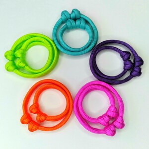 May include: Five colorful bracelets made of knotted rope. The bracelets are in shades of turquoise, lime green, purple, orange, and pink.