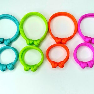 May include: Set of six colorful paracord bracelets with a knot design. The bracelets are turquoise, lime green, orange, pink, green, and purple.
