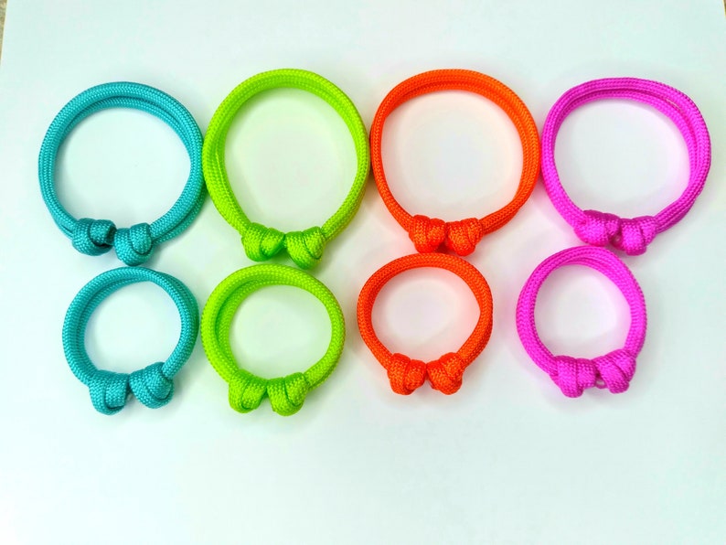 May include: Set of six colorful paracord bracelets with a knot design. The bracelets are turquoise, lime green, orange, pink, green, and purple.