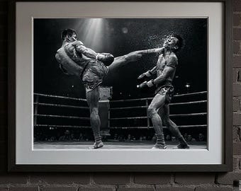 Könnte beinhalten: Ein schwarz-weiß gerahmtes Foto von zwei Muay-Thai-Kämpfern im Ring, von denen einer dem anderen einen hohen Tritt versetzt. Unter dem Rahmen liegen ein Paar braune Leder-Boxhandschuhe, zwei Glasflaschen und mehrere Rollen weißer Bandagen.