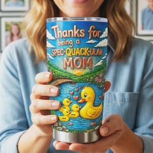 May include: Stainless steel tumbler with a colorful design. The tumbler features a duck pond scene with a mother duck and ducklings, a bridge, and the text "Thanks for being a SPEC-QUACK-ULAR MOM."