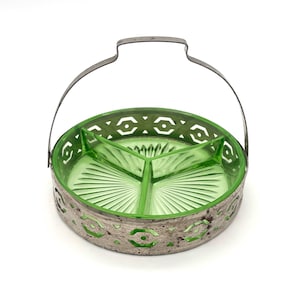 May include: A round, light green glass divided serving dish with three sections and a sunburst pattern on the base. The dish is encased in a weathered, silver-toned metal frame featuring a geometric cutout design and a tall, arched metal handle.