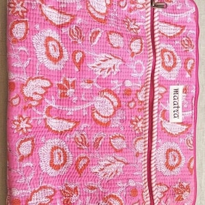 Op de afbeelding: Een rechthoekige gewatteerde laptoptas in felroze met een witte bloemen- en paisleyprint. Het heeft een verticaal zijvak met rits en een gestreepte bies, en een wit rechthoekig label met de tekst "maatra" op de voorzijde gestikt.