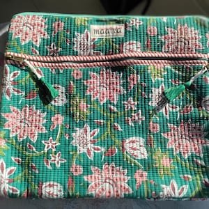Op de afbeelding: Een rechthoekige gewatteerde etui in groenblauw met een herhalend bloemenpatroon in roze en wit. De etui heeft een horizontaal ritsvak met een rood-witte gestreepte bies, twee groene kwastjes aan de ritstrekkers en een wit label met de tekst maatra.