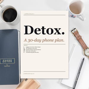 May include: A cream-colored paper with the word "Detox" in bold black letters, and the text "A 30-day phone plan." A navy blue notebook, a cup of coffee, a watch, and a pen are also visible.